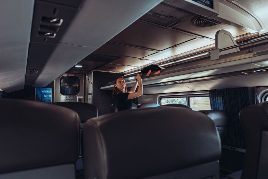 Female traveler stowing luggage in a train overhead compartment, emphasizing modern passenger travel.